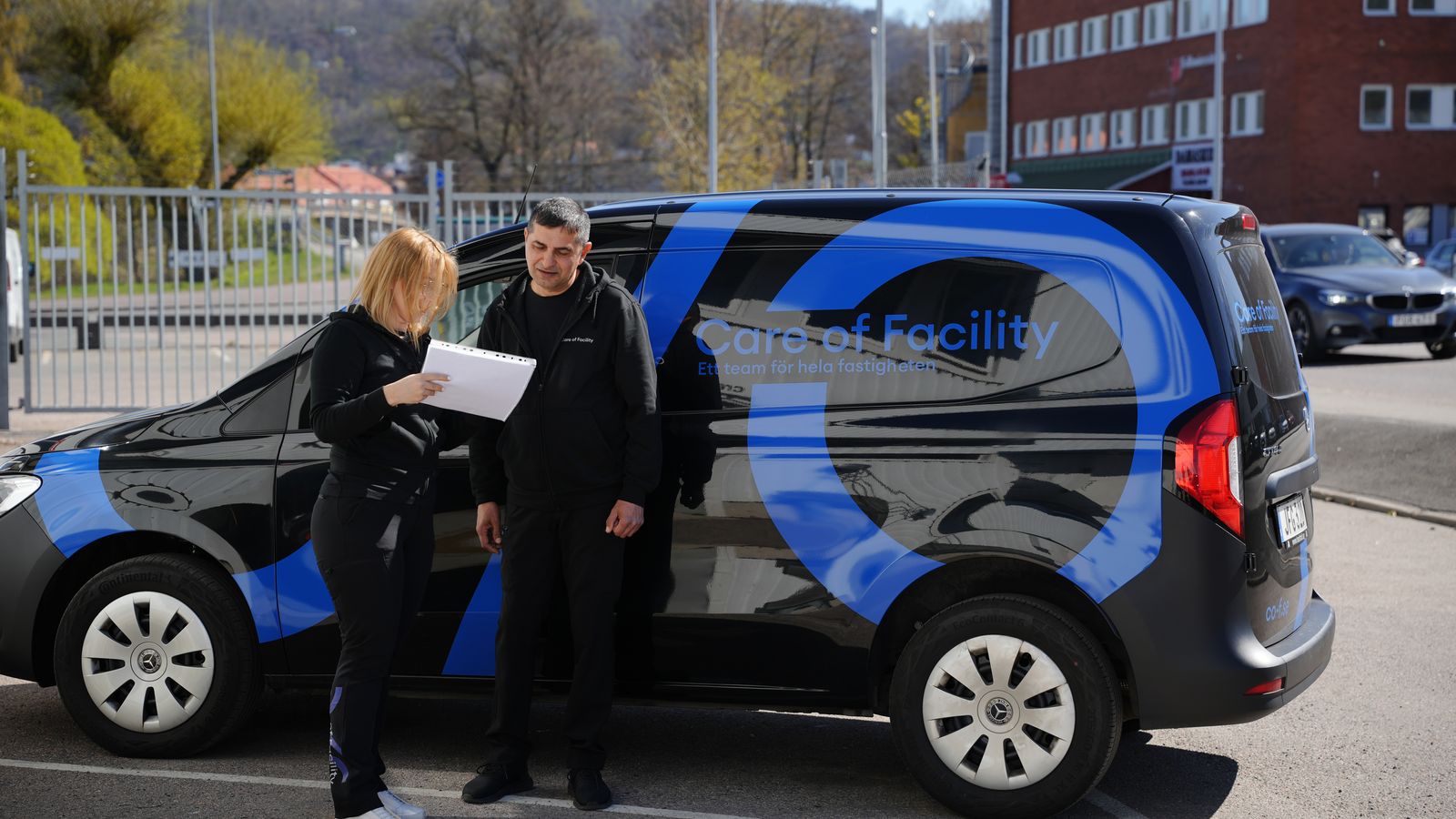 Två medarbetare från C/O Facility går igenom en checklista vid den profilerade firmabilen